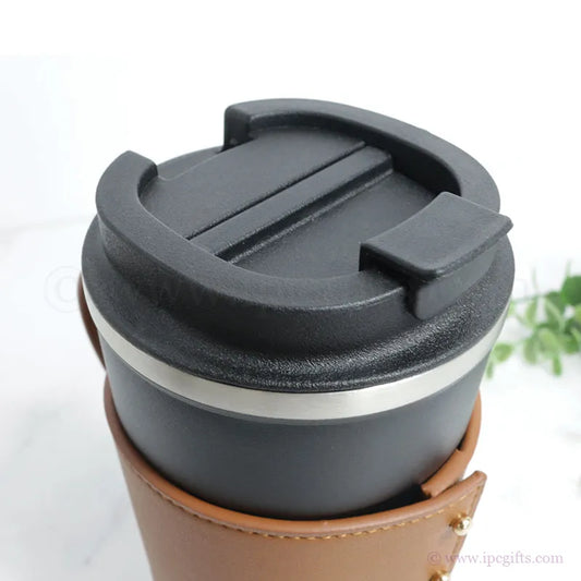 Black travel mug with a brown leather sleeve on a white background