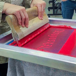 Person using a squeegee on a screen printing press with red ink
