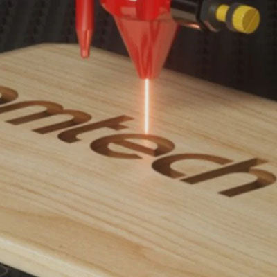 Laser engraving machine on a wooden surface with 'mtech' branding.