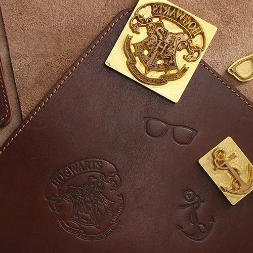 Close-up of a brown leather surface with debossed 'Hogwarts' logo and its respective embossing die (mold).